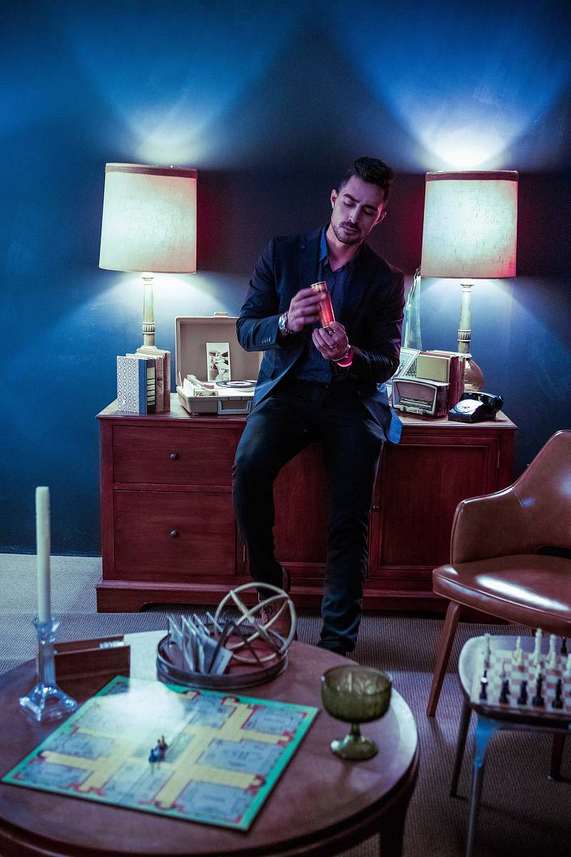 table lamp man sitting on lowboy dresser while holding glass of drink person
